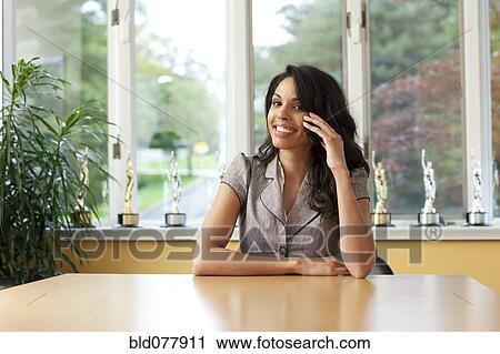 Stock Image - Hispanic woman talking on cell phone in dining room. Fotosearch