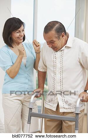 Stock Image - Hispanic woman watching husband use walker. Fotosearch