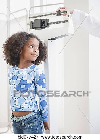 Stock Photo - Mixed race girl being weighed at doctor's office. Fotosearch