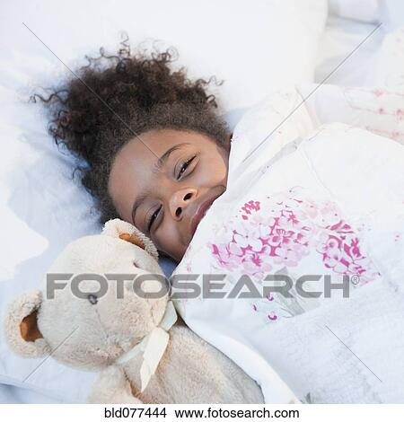 Picture - Mixed race girl in bed with teddy bear. Fotosearch