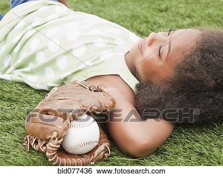 Stock Photograph - Mixed race girl laying next to baseball glove and ball. Fotosearch