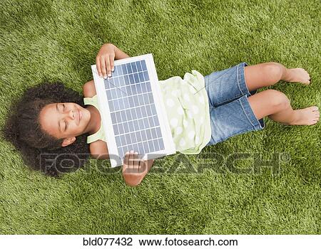 Stock Image - Mixed race girl laying with solar panel. Fotosearch