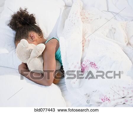Stock Image - Mixed race girl sleeping with teddy bear. Fotosearch