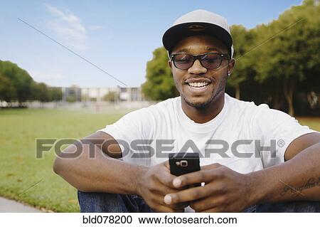 Stock Image - African American man in park using cell phone. Fotosearch