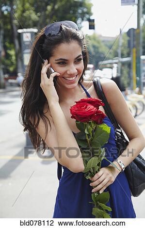 Stock Image - Brazilian woman holding red roses and talking on cell phone. Fotosearch