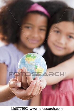 Stock Image - Girls holding globe together. Fotosearch