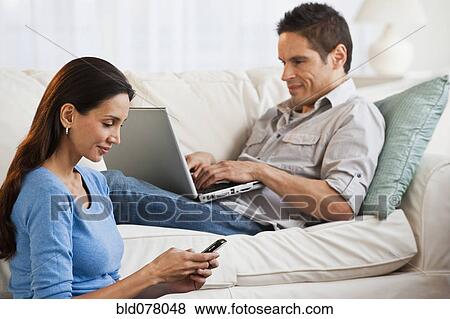 Stock Photo - Hispanic couple with laptop and cell phone in living room. Fotosearch