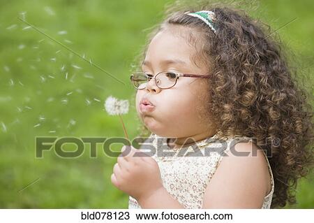 Stock Image - Hispanic girl blowing dandelion. Fotosearch