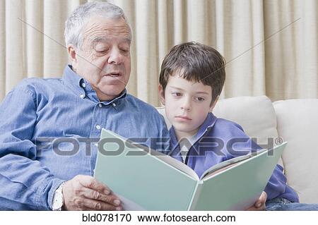 Stock Image - Hispanic grandfather reading book to grandson. Fotosearch