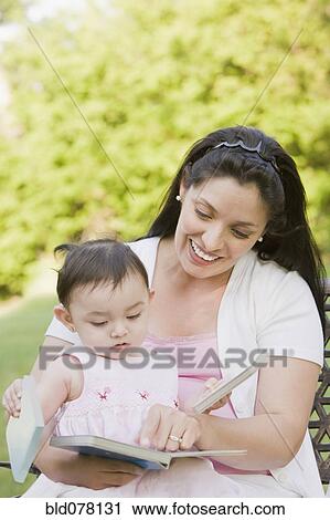 Stock Image - Hispanic mother reading to daughter. Fotosearch