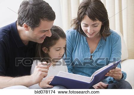 Picture - Hispanic parents reading book to daughter. Fotosearch