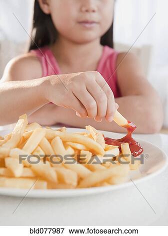 Stock Photo - Mixed race girl eating French fries and ketchup. Fotosearch