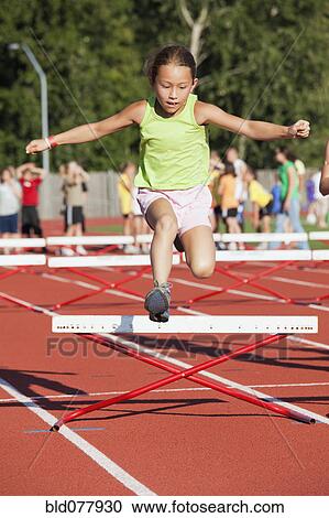 Stock Image - Mixed race girl jumping over hurdle. Fotosearch