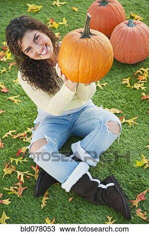 Stock Image - Mixed race woman holding pumpkin. Fotosearch