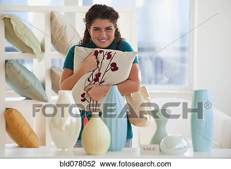Stock Image - Mixed race woman shopping for pillows. Fotosearch
