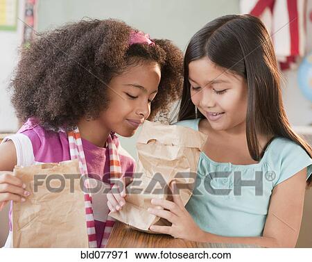 Stock Image - School girls looking into lunch bag. Fotosearch