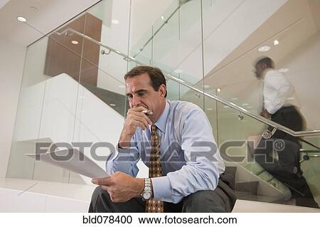 Businessman reviewing paperwork in office lobby View Large Photo Image Stock Image - Businessman reviewing paperwork in office lobby. Fotosearch