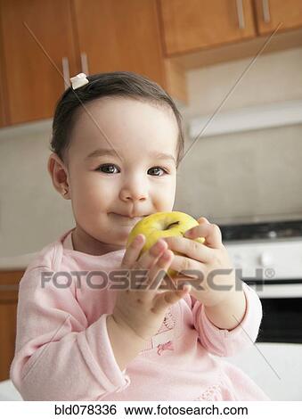 Stock Photograph - Hispanic baby girl eating apple. Fotosearch