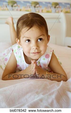 Stock Image - Hispanic girl praying on bed. Fotosearch