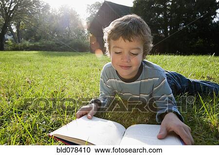 Stock Image - Mixed race boy reading book in grass. Fotosearch