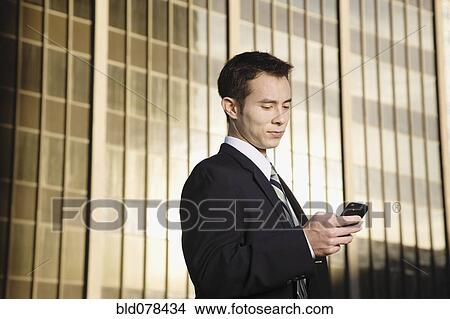 Picture - Mixed race businessman text messaging on cell phone. Fotosearch