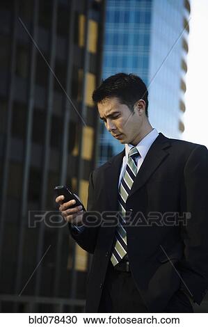 Stock Image - Mixed race businessman text messaging on cell phone. Fotosearch