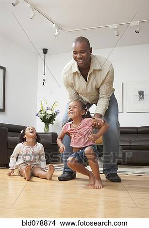 Picture - African American father playing with daughters in living room. Fotosearch