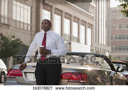 Stock Image - Black businessman drinking coffee near convertible. Fotosearch
