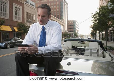 Caucasian businessman sitting on car text messaging on cell phone View Large Photo Image Stock Image - Caucasian businessman sitting on car text messaging on cell phone. Fotosearch