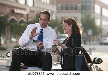 Stock Photography - Caucasian businessman sitting on car text messaging with co-worker. Fotosearch