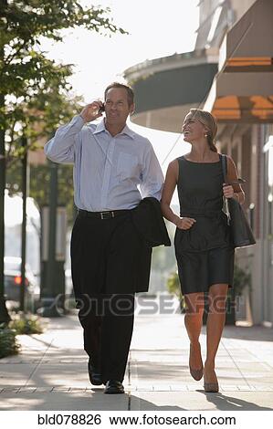 Stock Photograph - Caucasian businessman talking on cell phone and walking with co-worker. Fotosearch