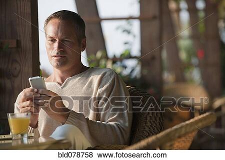 Stock Photo - Caucasian man text messaging on cell phone in restaurant. Fotosearch
