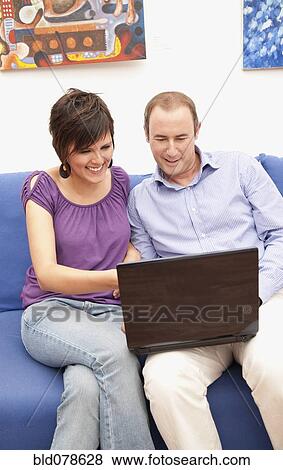 Stock Photo - Couple on sofa using laptop together. Fotosearch