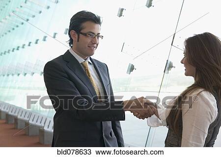Stock Image - Hispanic businessman shaking businesswoman's hand. Fotosearch
