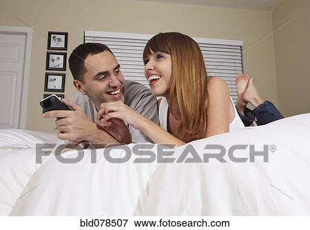 Stock Photo - Hispanic husband and wife watching television in bedroom. Fotosearch