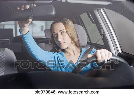 Stock Photograph - Hispanic woman adjusting rearview mirror. Fotosearch