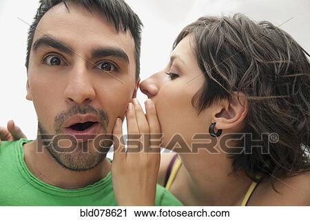 Stock Image - Hispanic woman whispering to boyfriend. Fotosearch