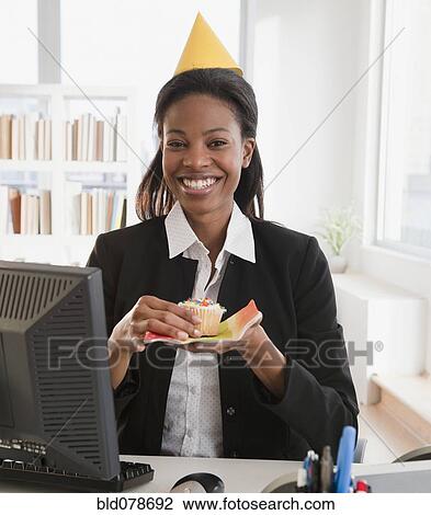 Stock Image - Mixed race businesswoman eating birthday cupcake. Fotosearch