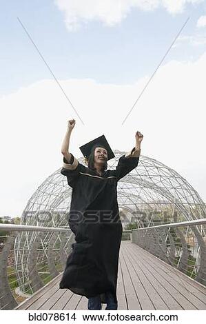 Picture - Mixed race graduate in cap and gown cheering. Fotosearch