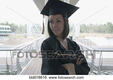 Stock Photograph - Mixed race graduate in cap and gown with arms crossed. Fotosearch