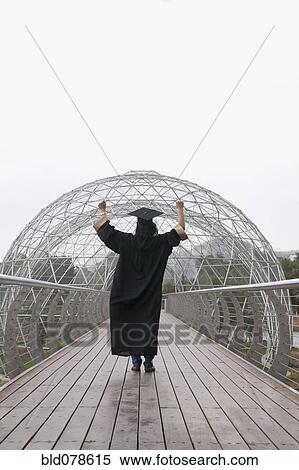 Stock Photography - Mixed race graduate in cap and gown cheering. Fotosearch