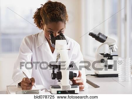 Stock Photography - Mixed race scientist peering into microscope. Fotosearch