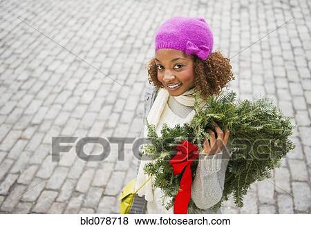 Mixed race woman carrying Christmas wreath View Large Photo Image Stock Photo - Mixed race woman carrying Christmas wreath. Fotosearch
