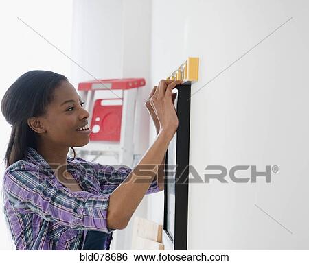 Stock Photograph - Mixed race woman hanging picture. Fotosearch