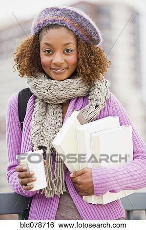 Stock Photograph - Mixed race woman holding books and drinking coffee. Fotosearch