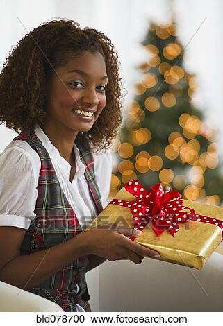 Stock Image - Mixed race woman holding Christmas gift. Fotosearch