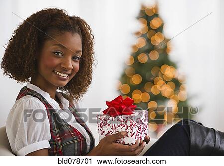 Stock Image - Mixed race woman holding Christmas gift. Fotosearch
