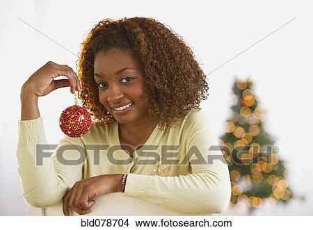 Picture - Mixed race woman holding Christmas ornament. Fotosearch