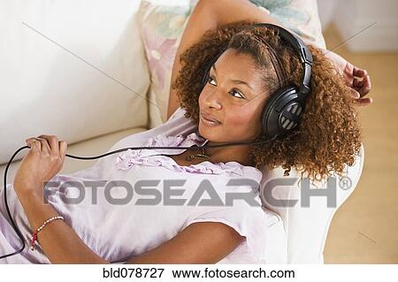 Stock Photo - Mixed race woman laying on sofa and listening to headphones. Fotosearch
