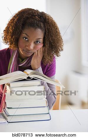 Stock Image - Mixed race woman looking at stack of books. Fotosearch